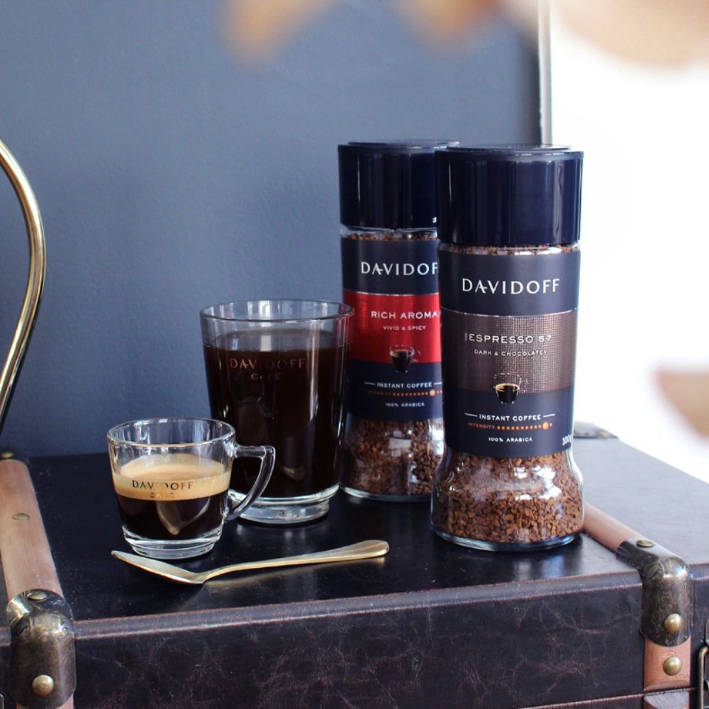 A jar of Rich Aroma next to a jar of Espresso 57 with a cup of each variety beside them.