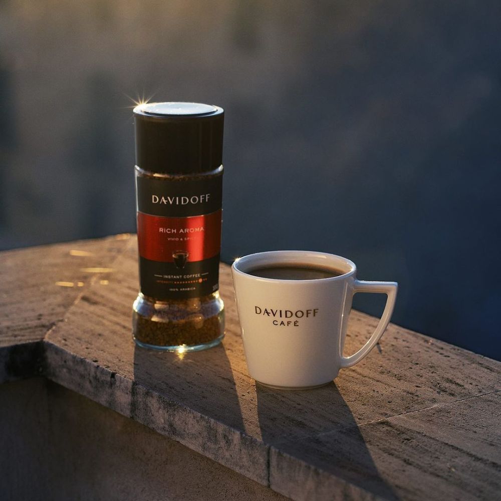 A jar of Rich Aroma sitting next to a cup of prepared coffee on an outdoor ledge.