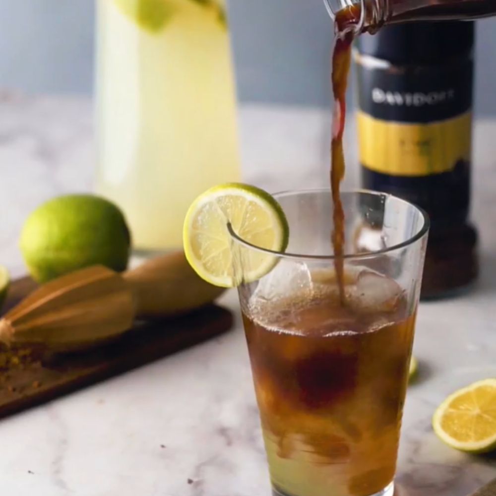 A picture of prepared Fine Aroma coffee being added to ice in a glass with a lemon slice.