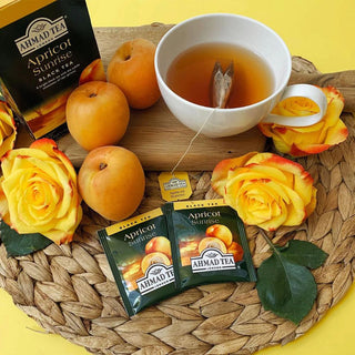 Ahmad Apricot Sunrise tea brewed in a cup with tea bags and apricots beside on a table